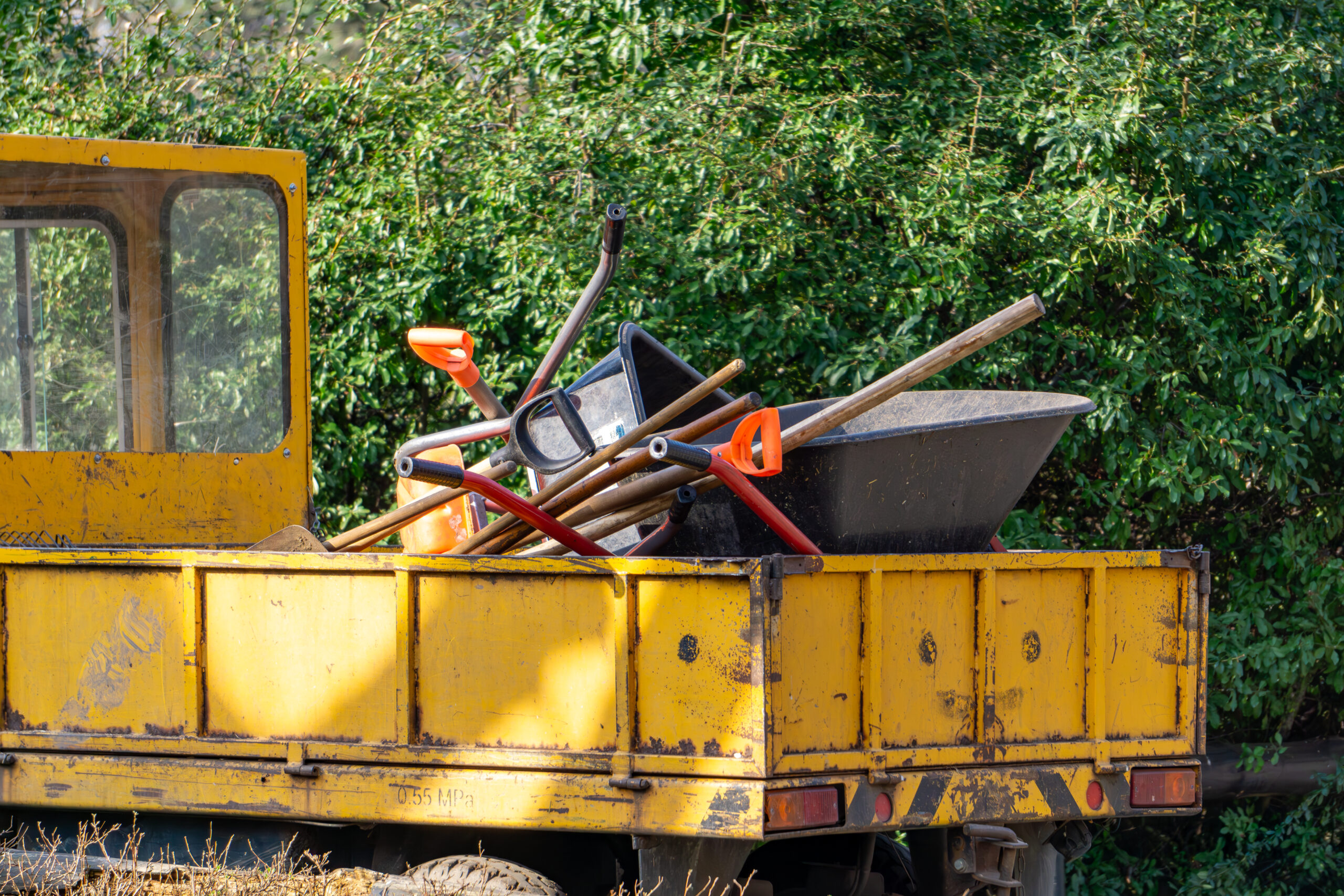 A small landscaping truck with gardening tools piled up in the back such as shovels, rakes, and a wheelbarrow